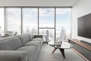 A modern living room with a grey sectional sofa, a round coffee table, and a large TV on the wall. - Sky High 2BR With Spectacular City Views (Melbourne)