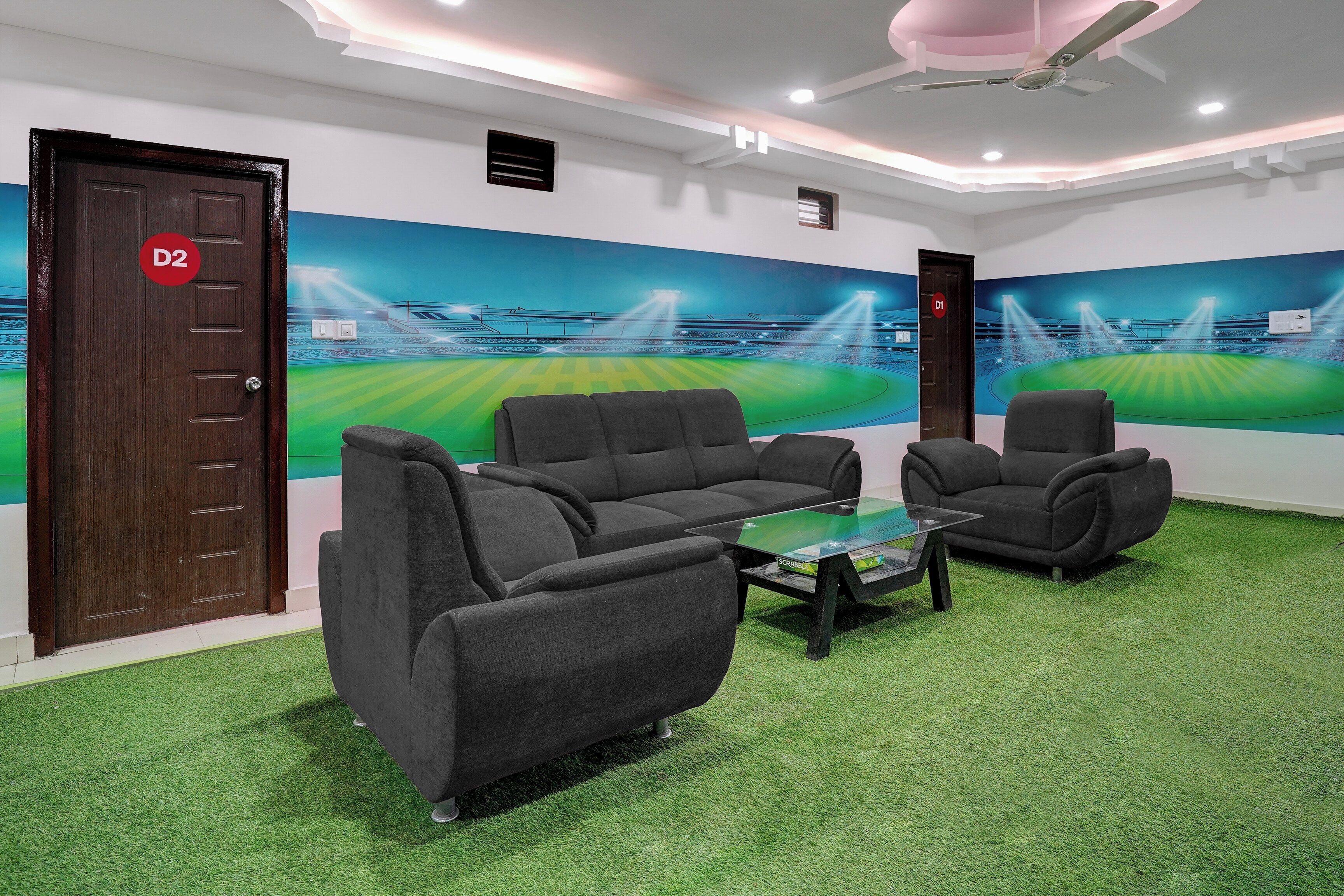 Una habitación con alfombra verde, sofás grises, una mesa de centro de vidrio y un mural en la pared de un estadio.