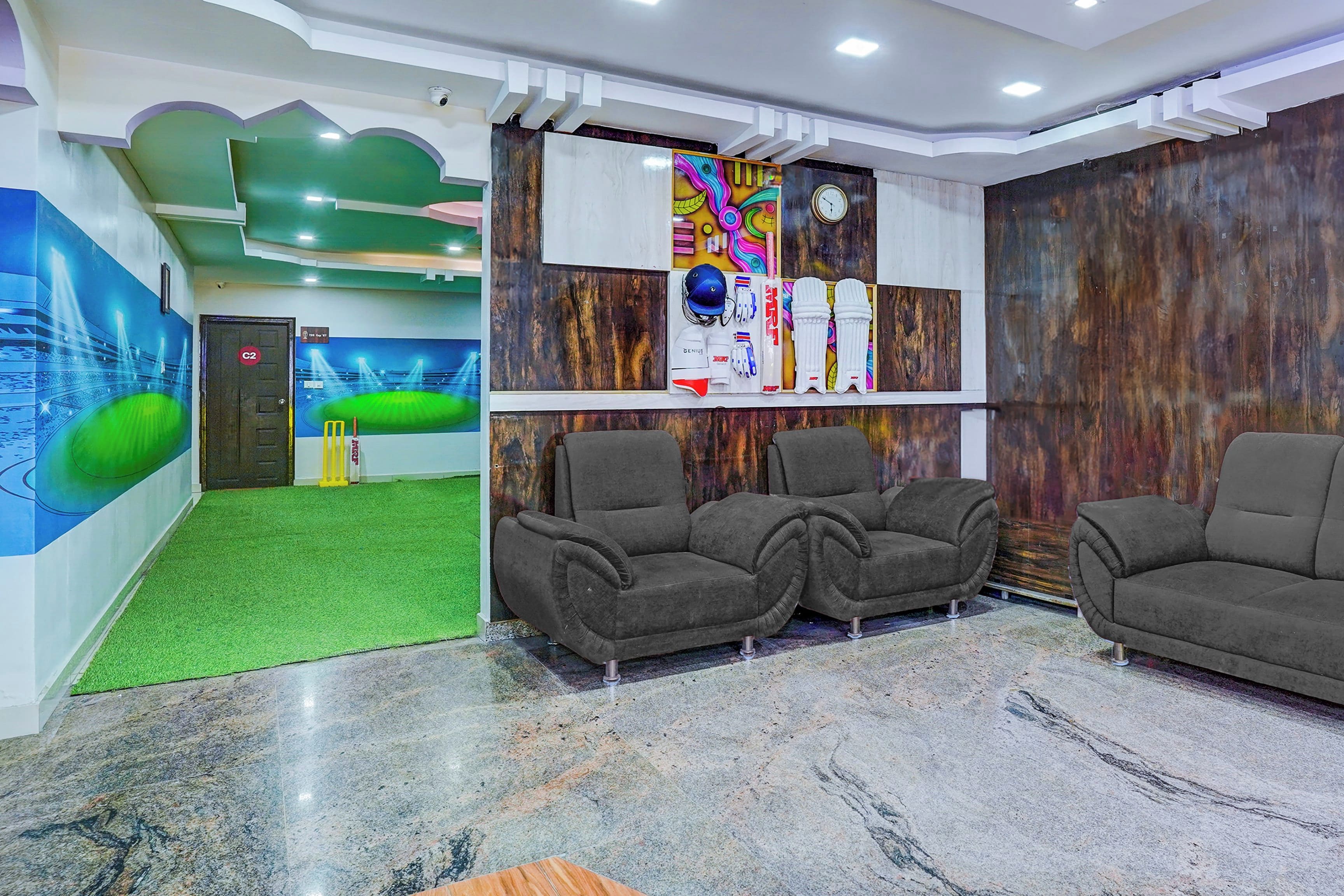 A reception area with a green carpet, grey sofas, a cricket set, and a mural of a stadium.