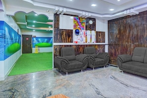 A reception area with a green carpet, grey sofas, a cricket set, and a mural of a stadium.