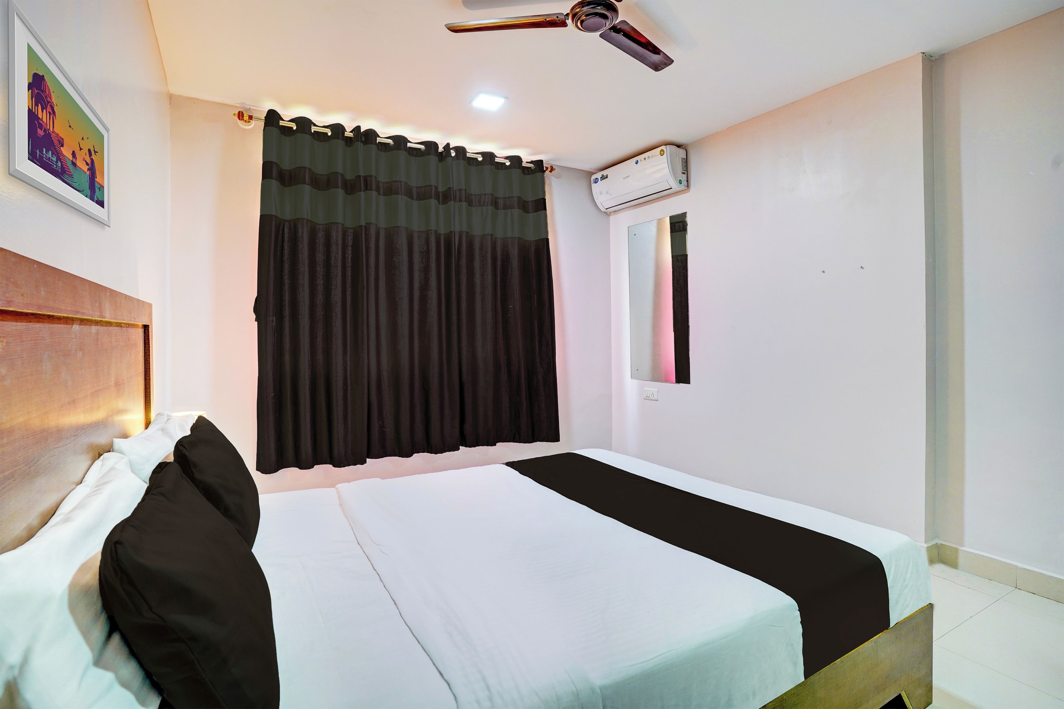 Habitación de hotel con cama, ventilador de techo, unidad de aire acondicionado, ventana con cortina e imagen colgada en la pared.