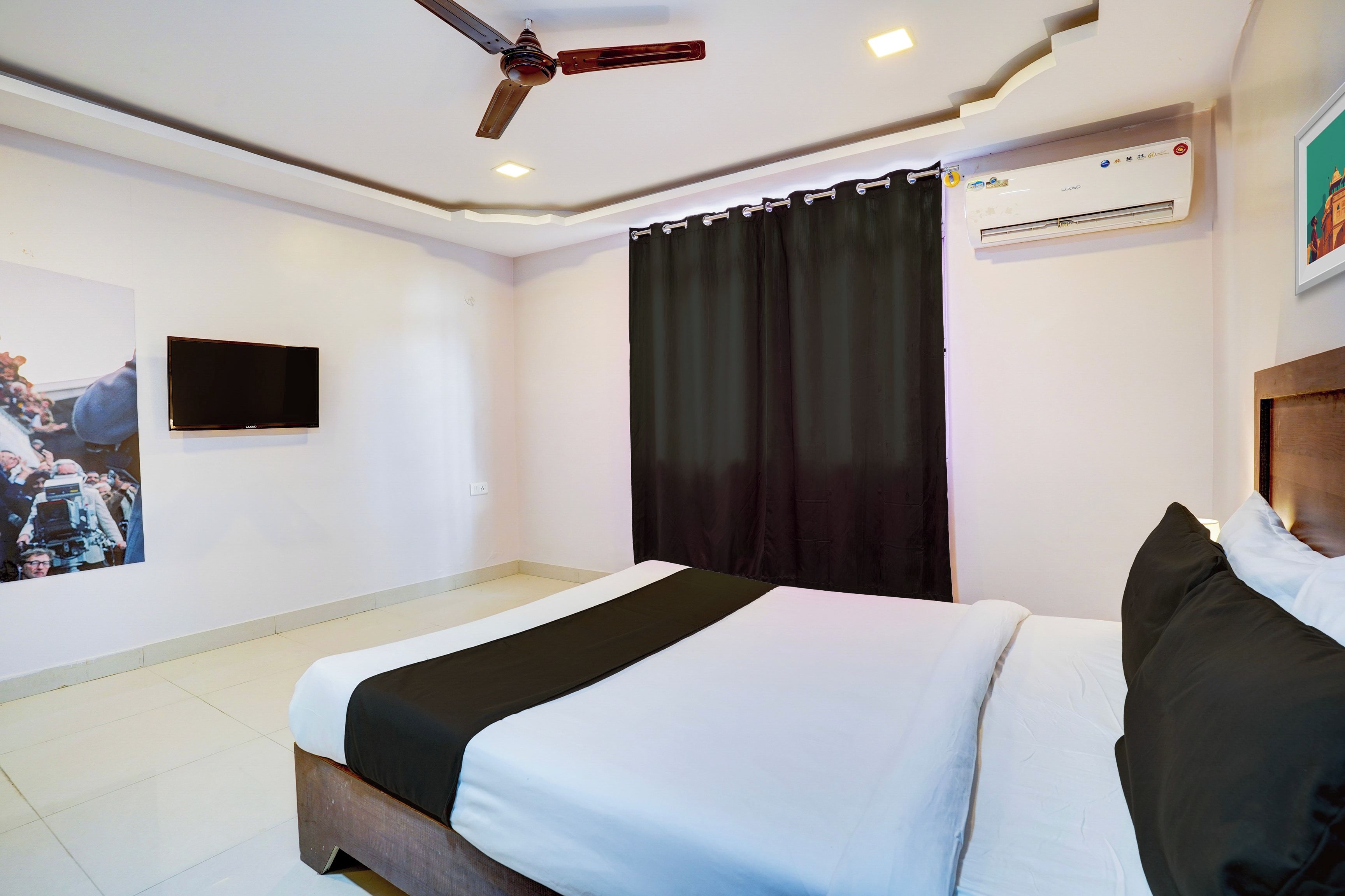 A hotel room with a bed, a ceiling fan, an air conditioning unit, a television mounted on the wall, and a curtain.