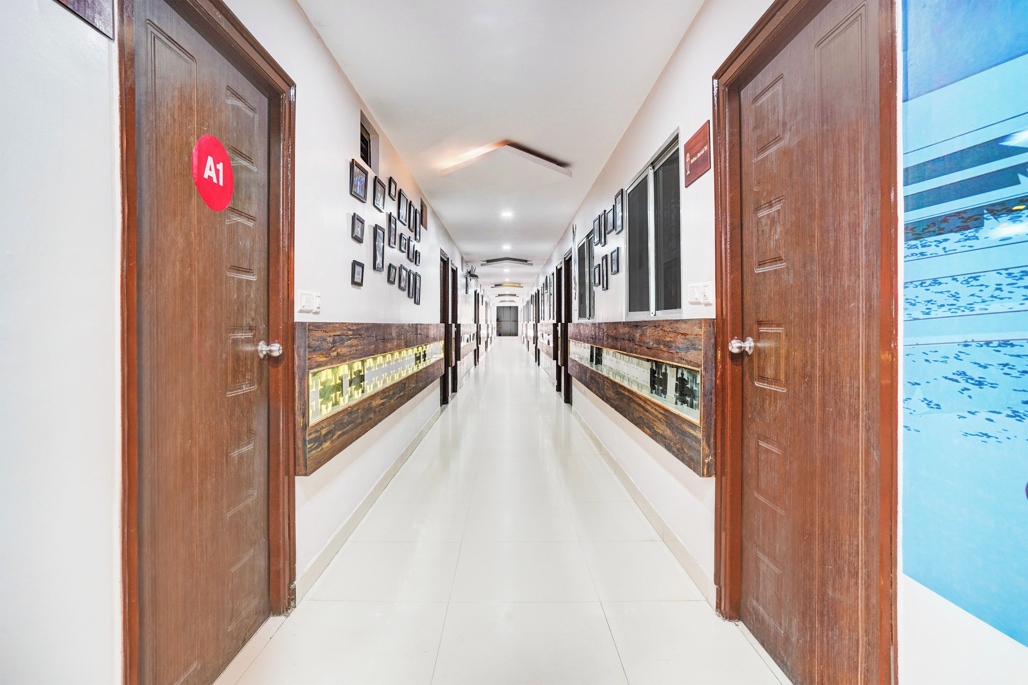 Pasillo de hotel con puertas de madera, un letrero rojo 'A1' y cuadros enmarcados en las paredes.
