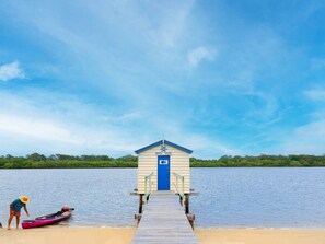 A wheelhouse on a wooden pier extending into a calm lake, with a kayak and a person near the dock. - Ingara @ Maroochydore (Maroochydore)