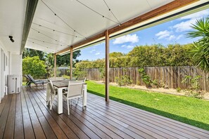 A covered outdoor patio with a wooden deck, a table, and chairs. - Ingara @ Maroochydore (Maroochydore)