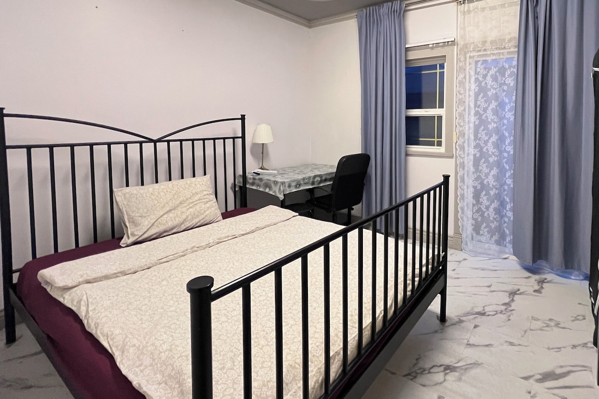 A bedroom with a single bed, a desk, and a window with curtains.