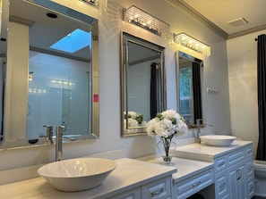 A bathroom with a large mirror, a white sink, and a vase of white flowers. - Haidian Mama Garden Suite (Richmond)