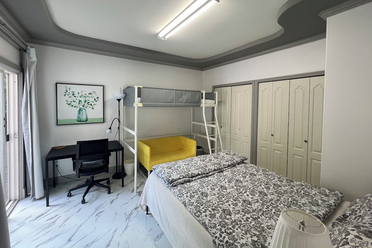 A bedroom with a bunk bed, a desk with a chair, a lamp, and a wardrobe.