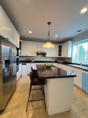 A modern kitchen with white cabinets, a stainless steel refrigerator, a central island with bar stools, and a pendant light. - Haidian Mama Garden Suite (Richmond)