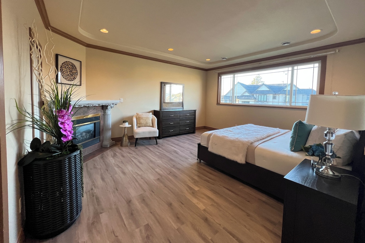 A bedroom with a bed, dresser, nightstand, and a fireplace.