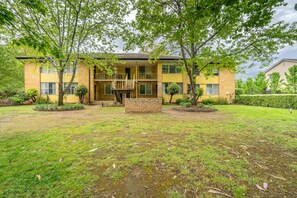 A two-story building with a brick facade, a front porch, and a small front yard with trees and shrubs.