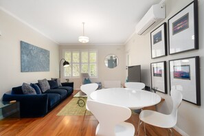 A modern living room with a dark blue sofa, white chairs, a round table, and artwork on the walls.