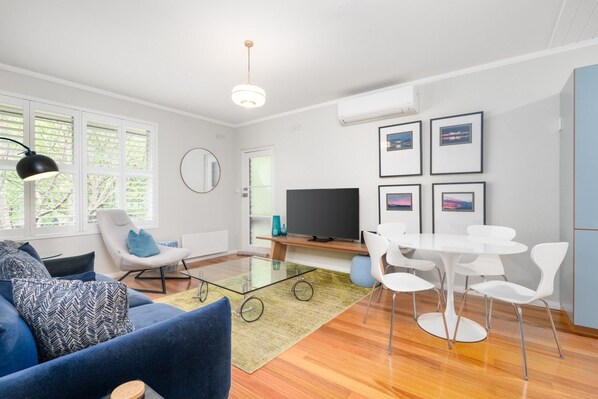 A modern living room with a sofa, chairs, a glass coffee table, a TV, and framed pictures on the wall.