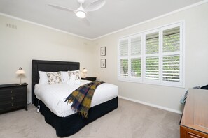A bedroom with a bed, bedside tables, a ceiling fan, a window with blinds, and a small desk.