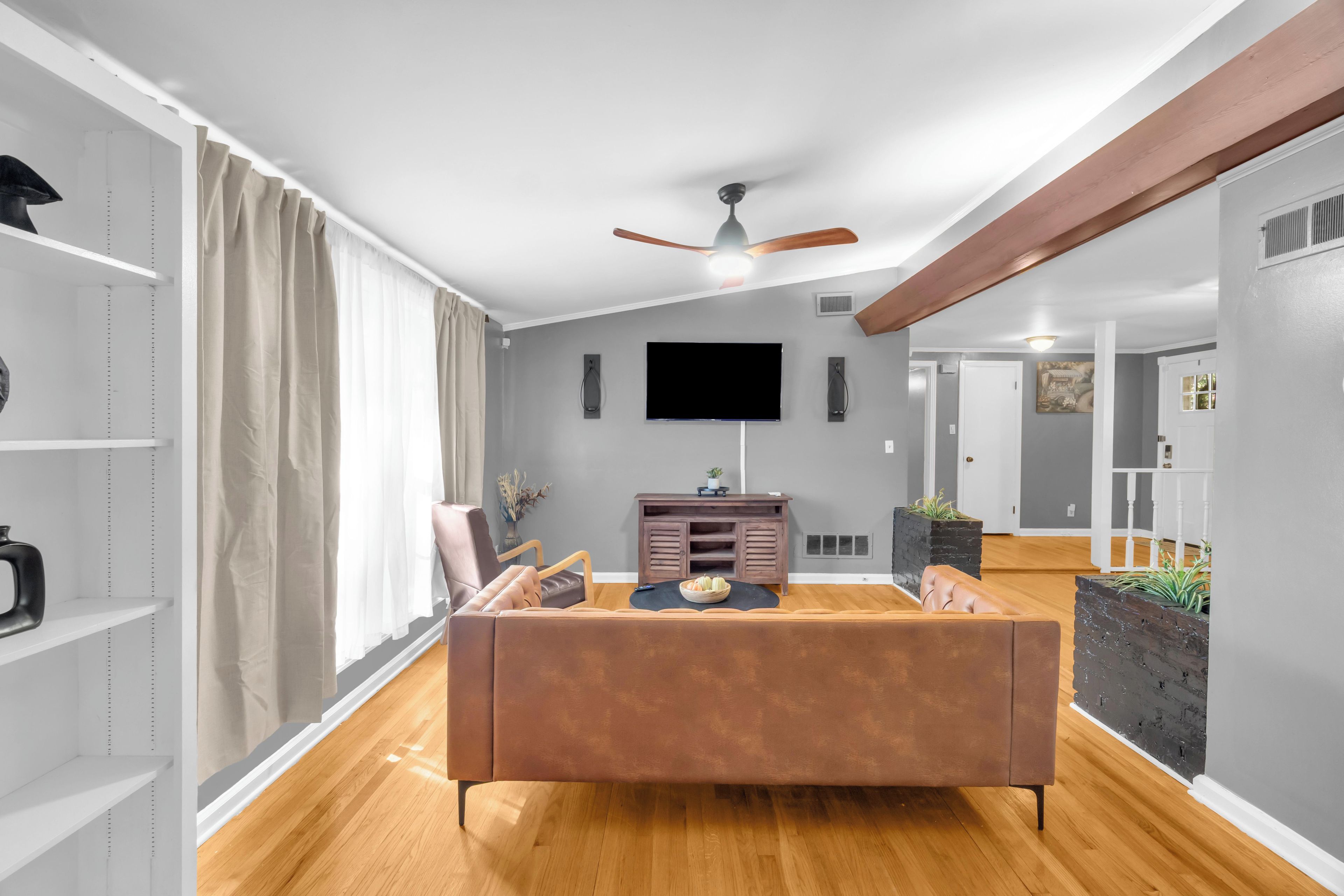 Una sala de estar moderna con un sofá marrón, un televisor de pantalla plana y un ventilador de techo.
