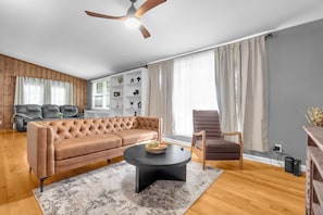 A modern living room with a brown leather sofa, a round coffee table, and a wooden floor. - Midtown Executive | Work & Extended Stays | 4 Beds (Montgomery)