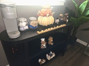 A coffee maker, jars, a pumpkin decoration, and small figurines on a black console table. - Midtown Executive | Work & Extended Stays | 4 Beds (Montgomery)