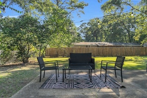 An outdoor seating area with a table and chairs, a patterned rug, and a wooden fence in the background. - Midtown Executive | Work & Extended Stays | 4 Beds (Montgomery)