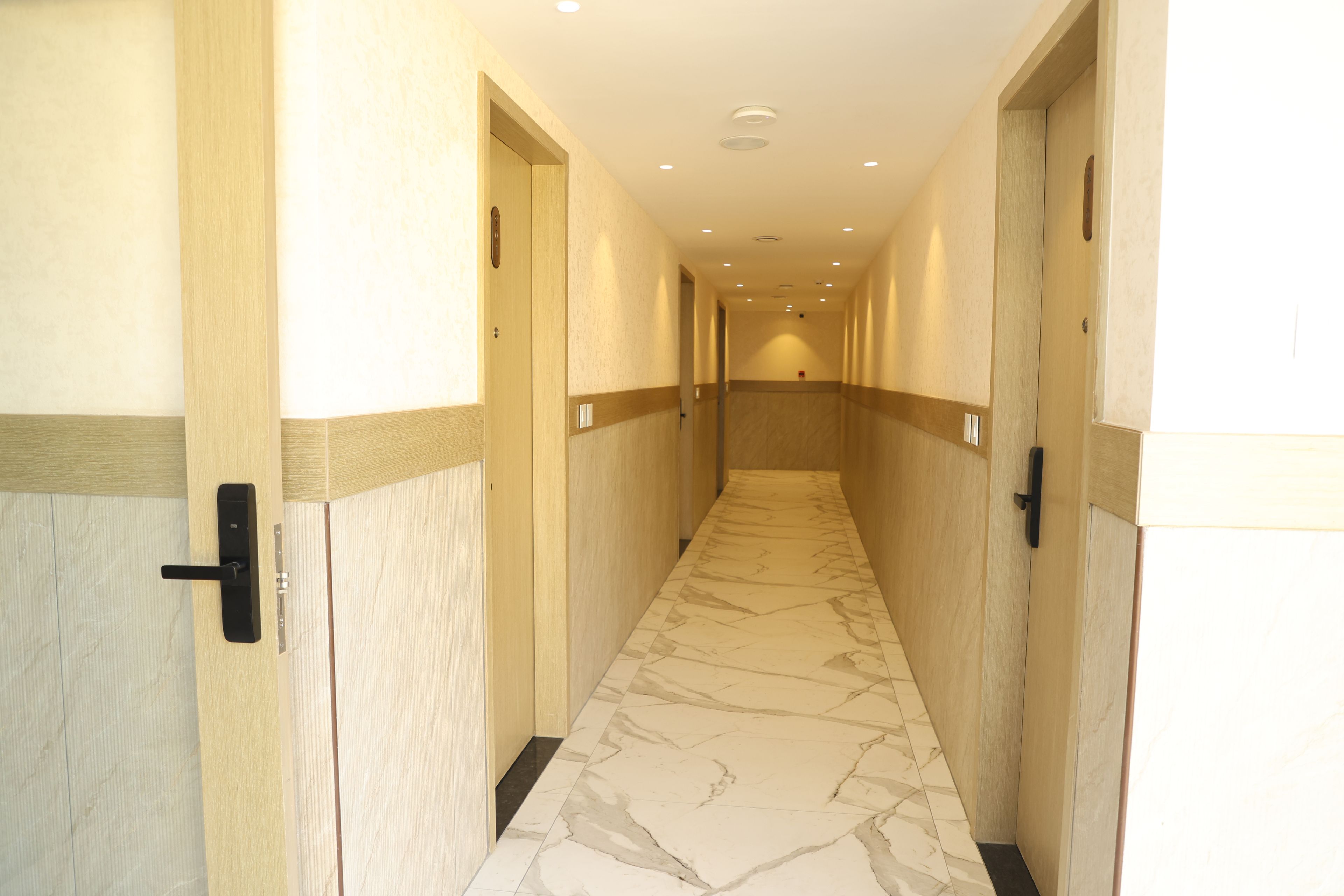 A hotel corridor with marble flooring, wooden doors, and recessed lighting.