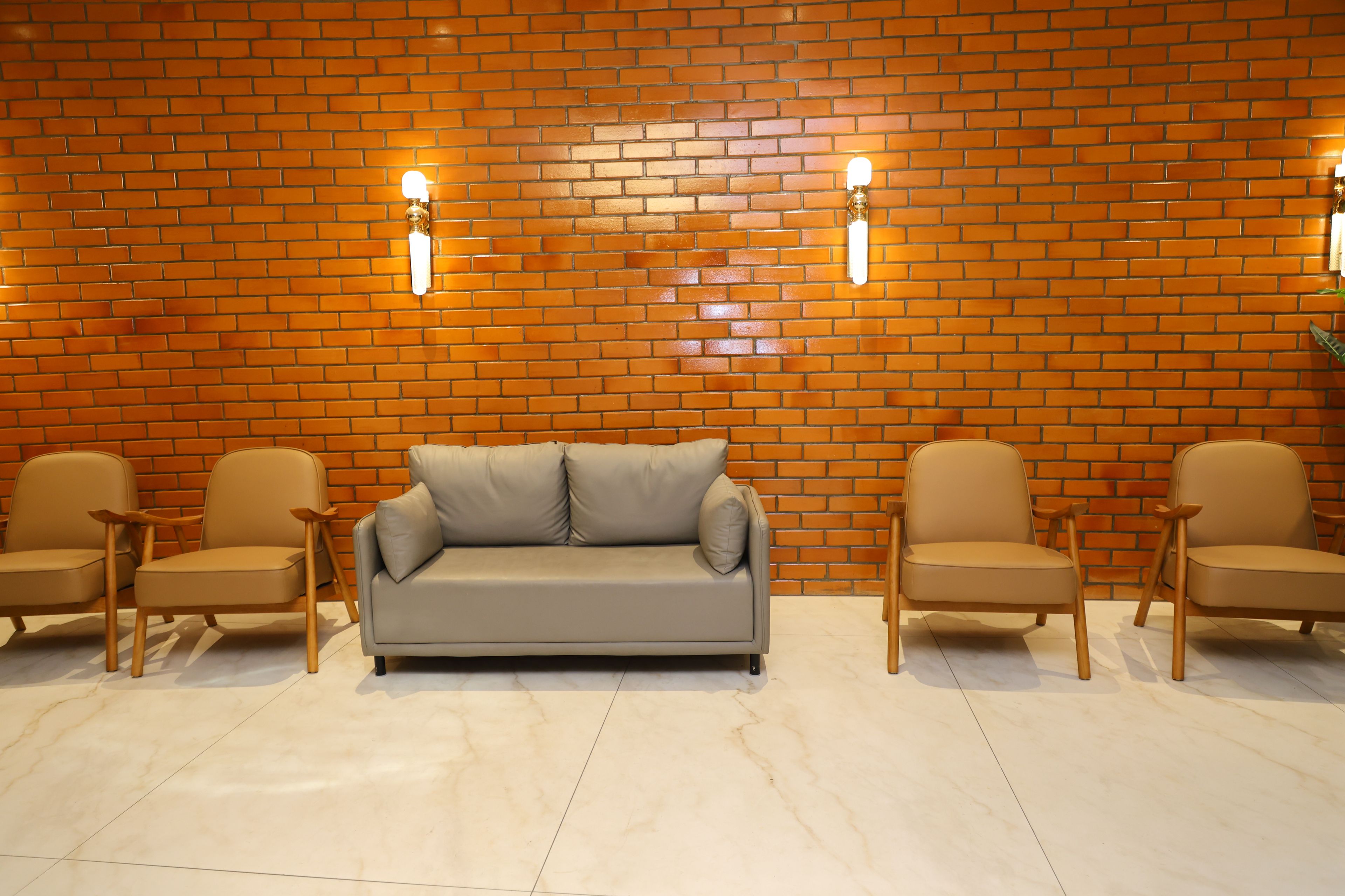 Una habitación con pared de ladrillo, un sofá gris y dos sillas de madera.