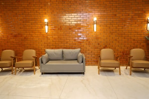 Una habitación con pared de ladrillo, un sofá gris y dos sillas de madera.