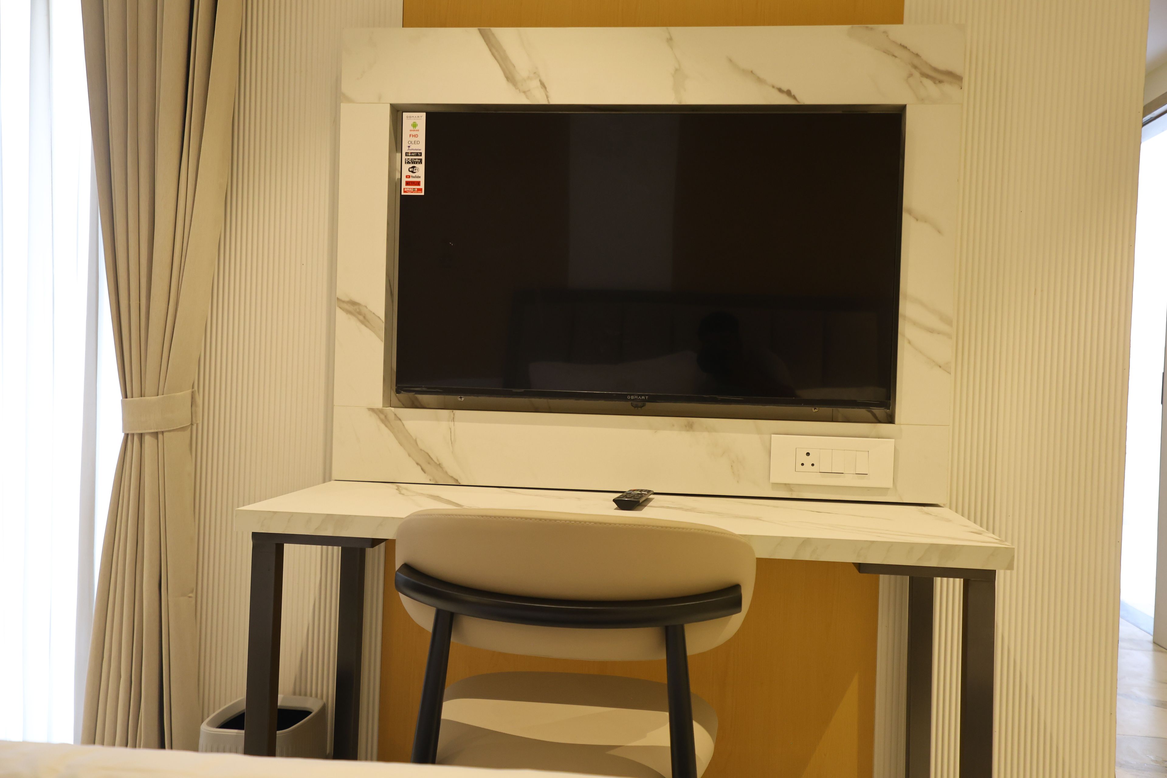 Una habitación moderna con pared de mármol, un televisor de pantalla plana sobre un escritorio y una silla.