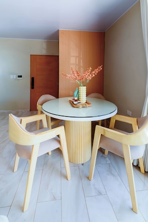 Un comedor con una mesa redonda de vidrio, cuatro sillas de madera, una puerta de madera e interruptor de luz en la pared.