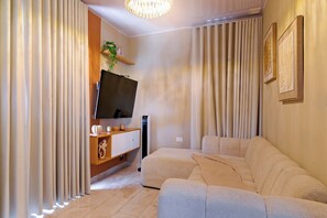 A modern living room with a sectional sofa, a flat-screen TV, a wooden entertainment unit, and a wall-mounted air conditioning unit. - Puerto Plata City Stay (Puerto Plata)