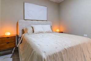 Un dormitorio con una cama, dos mesitas de noche, una lámpara de noche y una obra de arte en la pared.