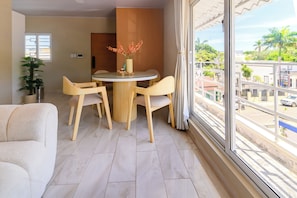 A modern living room with a round table, two chairs, a sofa, and a large window with a view of a residential area. - Puerto Plata City Stay (Puerto Plata)