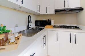 A modern kitchen with white cabinets, a stainless steel sink, a black faucet, a microwave, and a gas stove. - Puerto Plata City Stay (Puerto Plata)