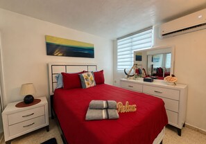 Une chambre à coucher avec une couvre-lit rouge, une table de chevet avec une lampe, une commode et un miroir.