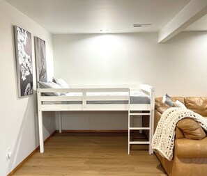 A room with a bunk bed, a wooden floor, a couch with a blanket, and two wall-mounted pictures. - The PNW Haven - Cozy 1-br Bottom unit in amazing Seattle neighborhood with AC. (Seattle)