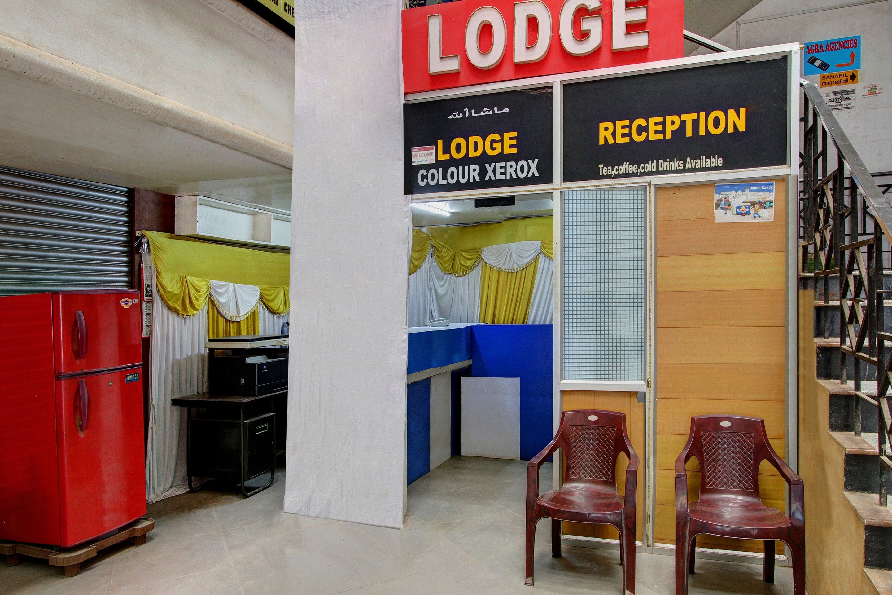 A reception area with a sign for 'Lodge Colour Xerox' and a 'Reception' sign indicating amenities like tea, coffee, and cold drinks. There are two wooden chairs and a red refrigerator in the room.