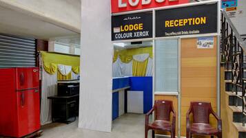 A reception area with a sign for 'Lodge Colour Xerox' and a 'Reception' sign indicating amenities like tea, coffee, and cold drinks. There are two wooden chairs and a red refrigerator in the room.