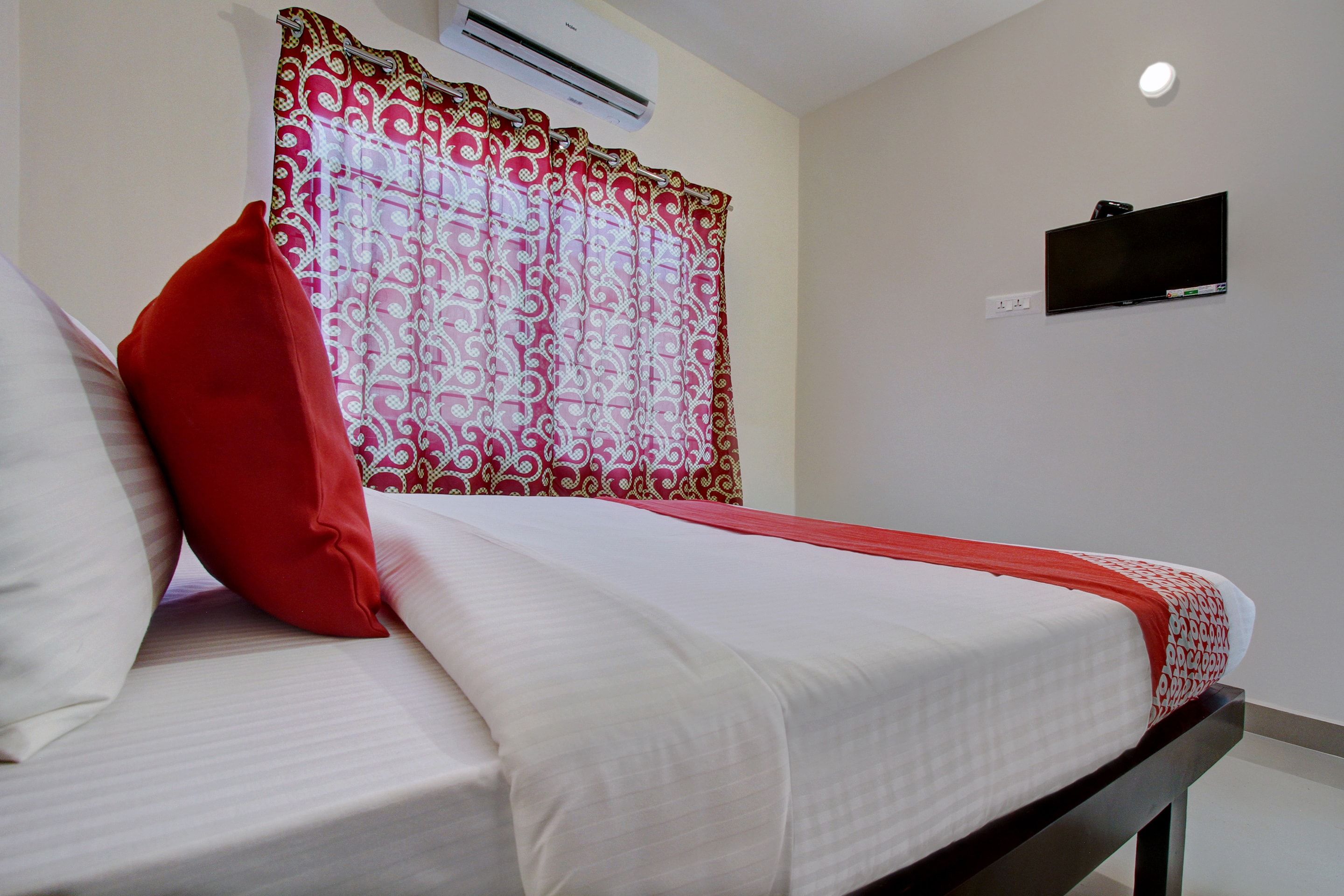 Habitación de hotel con cama, ventana con cortinas estampadas, equipo de aire acondicionado, televisor de pantalla plana y toma de corriente.