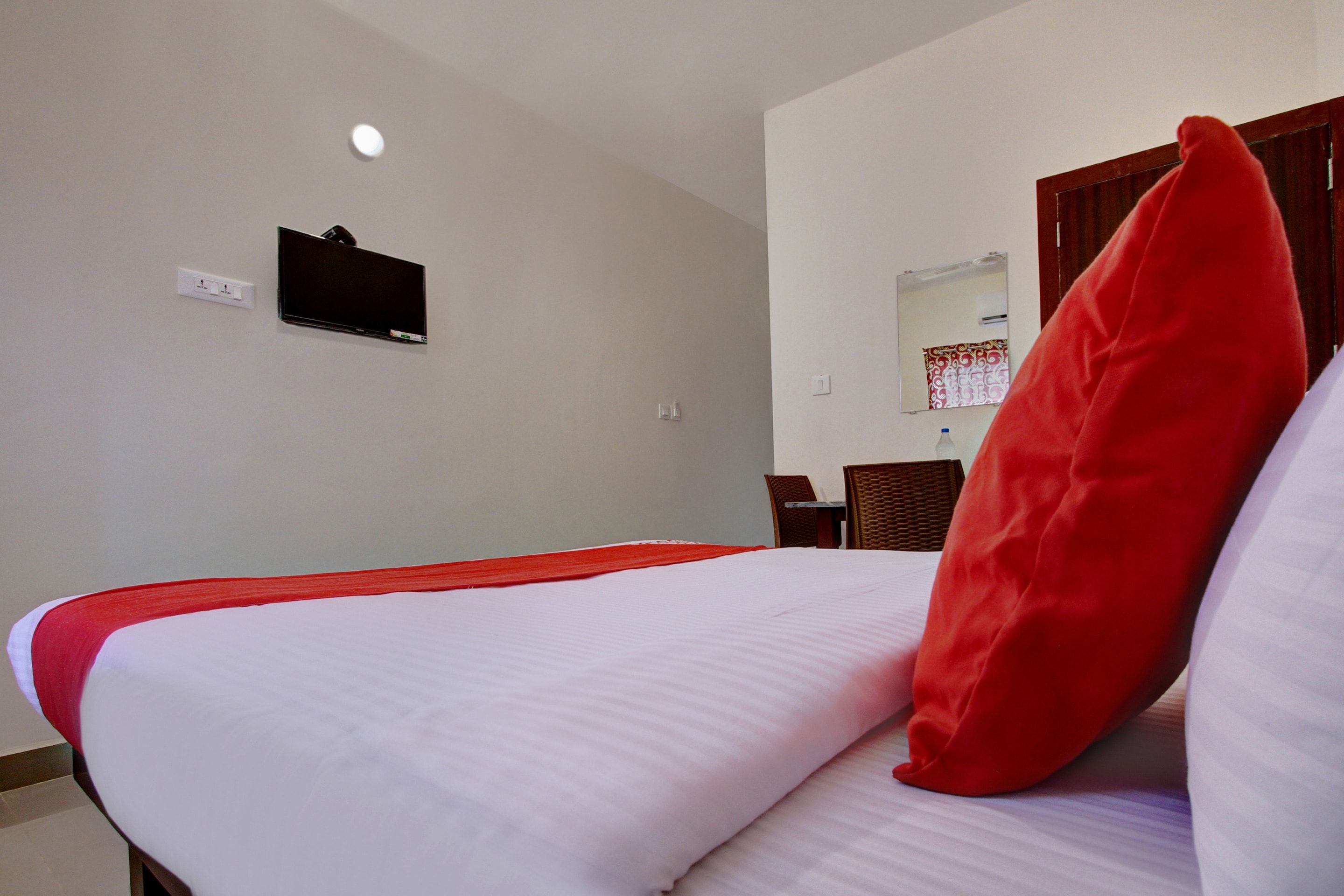 A hotel room with a bed, a television mounted on the wall, and a mirror above a wooden door.