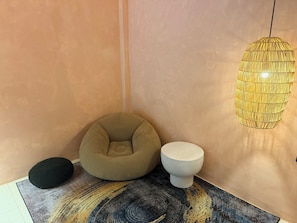 Eine Ecke eines Raumes mit einem beige-farbenen Sitzsack, einem kleinen weißen Tisch und einer Hängelampe.
