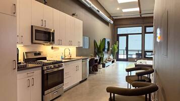 A modern kitchen with stainless steel appliances, a dining area with bar stools, and large windows providing natural light.