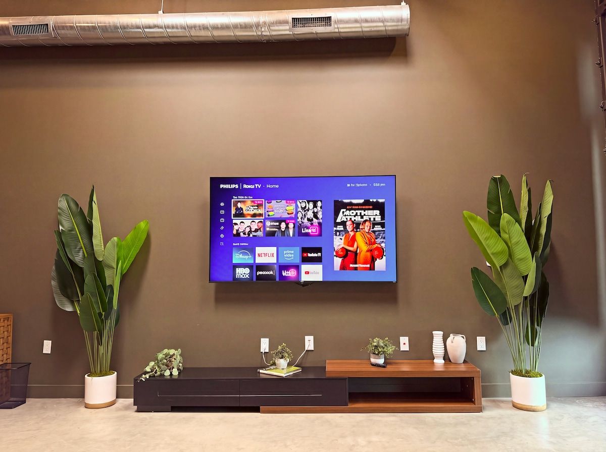 Ein an der Wand befestigtes Fernsehgerät zeigt einen Homescreen mit verschiedenen Streaming-Diensten.