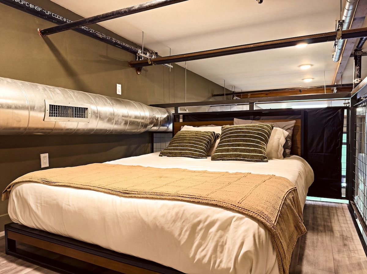 A bedroom with a bed, pillows, a blanket, and a visible ductwork system.