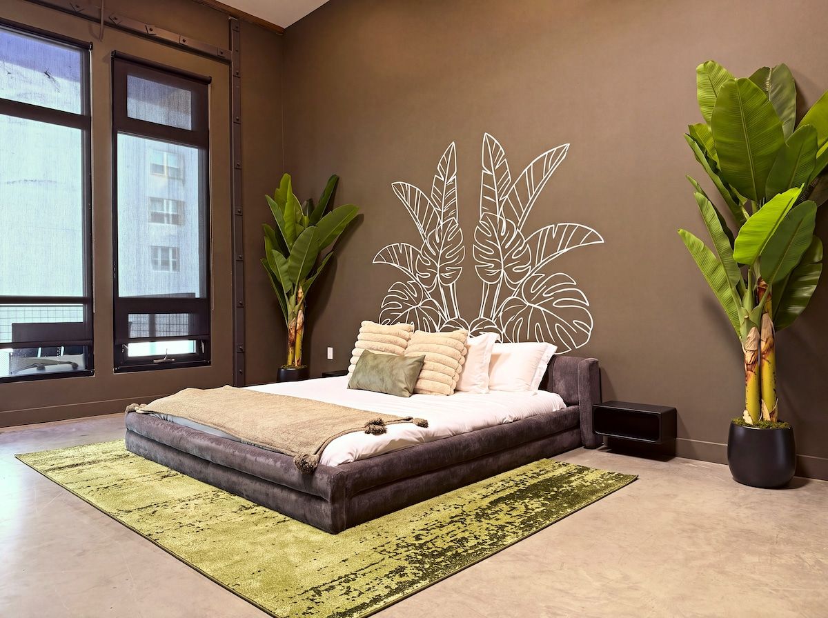 Un dormitorio moderno con una cama grande, dos plantas en macetas y vistas por la ventana.