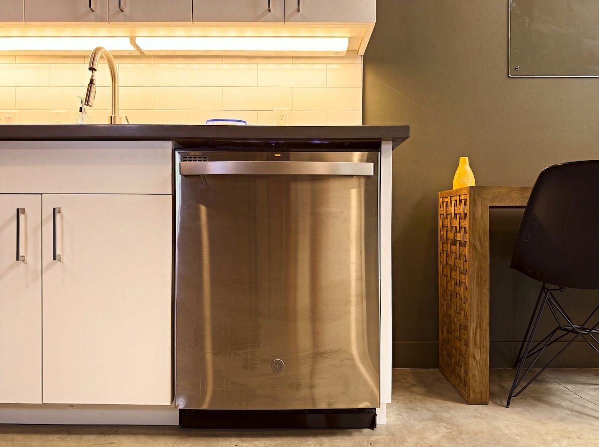 A kitchen with a stainless steel dishwasher, a wooden sideboard, and a black chair.