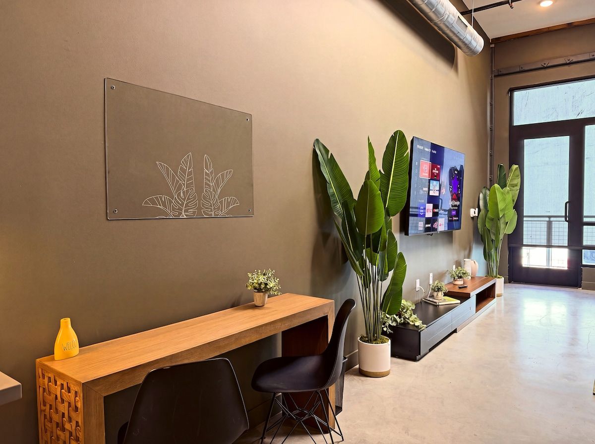 A reception area with a wooden desk, black chairs, a wall-mounted screen, and potted plants.