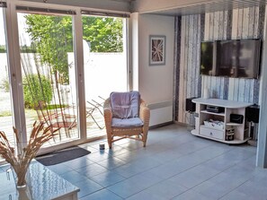 A room with a wicker chair, a flat-screen TV, and a tiled floor. - mit Grill und Garten in Neukirchen by Interhome (Kraksdorf)