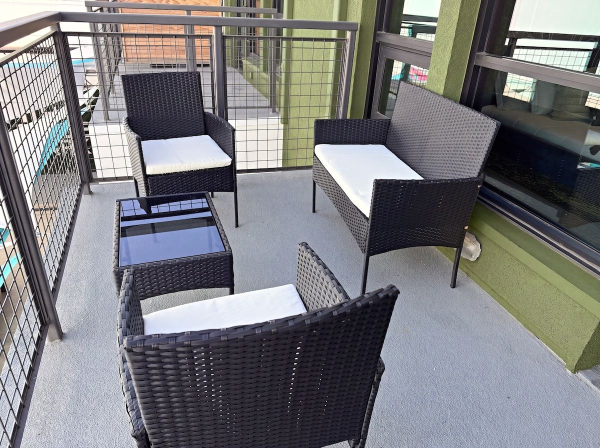 A balcony with wicker furniture, including two chairs and a table, and a glass partition.
