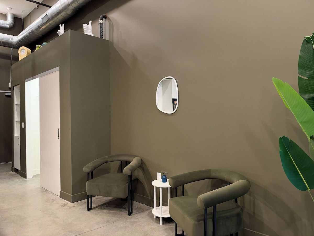 A room with two armchairs, a small table, a mirror, and a door.