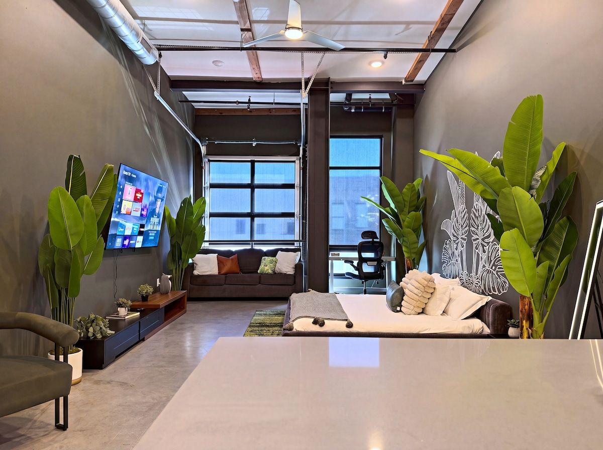 Un interior moderno con sofá, cama, televisor y plantas verdes grandes.