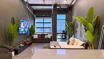 Un interior moderno con sofá, cama, televisor y plantas verdes grandes.