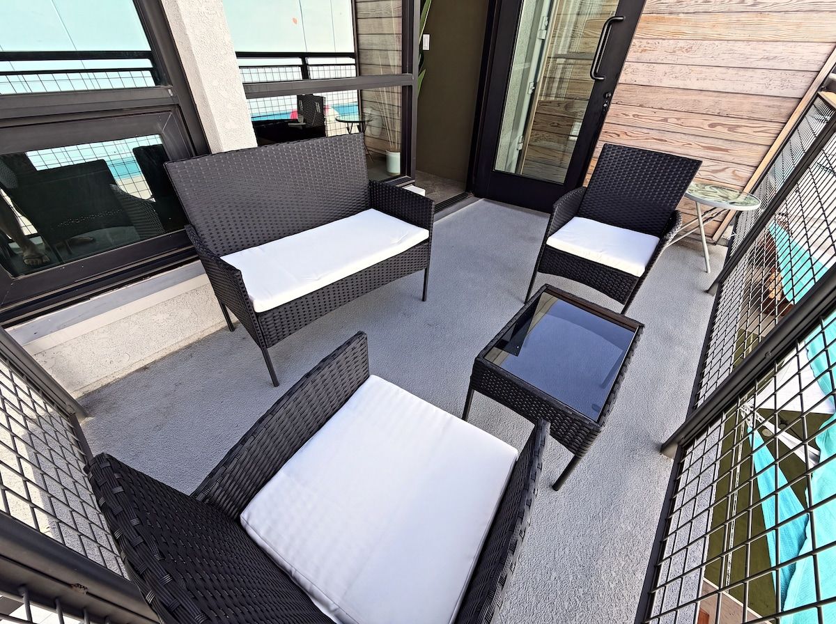 A balcony with wicker furniture, a glass table, and a view of the building's exterior.